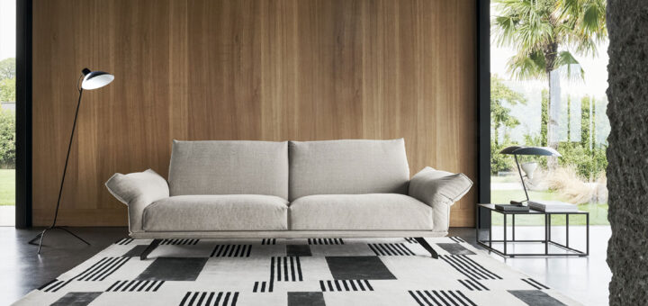 Divano Wing di Twils dalle linee essenziali in un living con parete in legno e tappeto geometrico