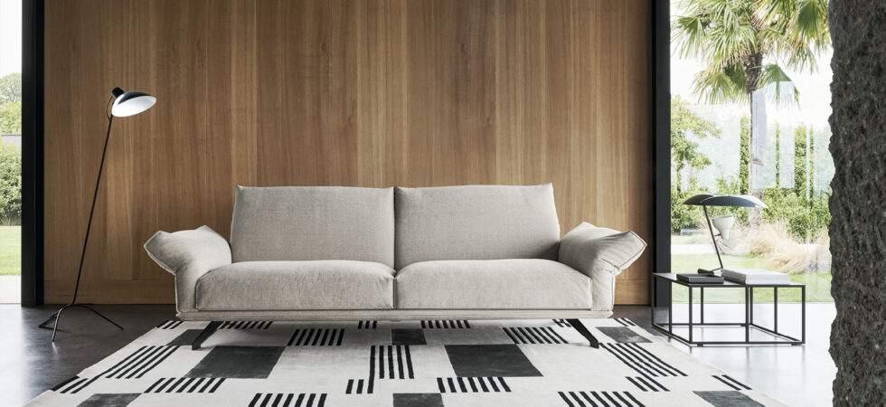 Divano Wing di Twils dalle linee essenziali in un living con parete in legno e tappeto geometrico