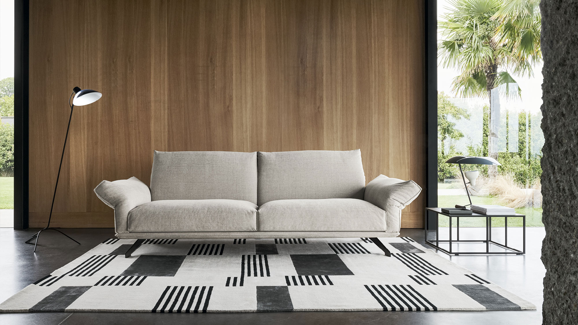 Divano Wing di Twils dalle linee essenziali in un living con parete in legno e tappeto geometrico